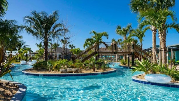 Ein Resort-Poolbereich mit mehreren Wasserrutschen, Palmen und einer Brücke.
