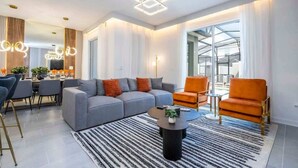 Ein modernes Wohnzimmer mit einer Couch, Sesseln, einem Couchtisch und einem Essbereich mit Stühlen und einem Tisch.