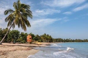 Una playa con una torre de salvavidas, palmeras y cielo despejado.