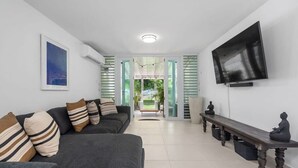 A modern living room with a grey sofa, a flat-screen TV, and a meditation bench.