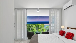 A hotel room with a bed, a balcony with a view, and an air conditioning unit.