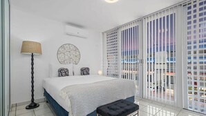 A bedroom with a bed, a floor lamp, a round wall decoration, and a view through a window with blinds.