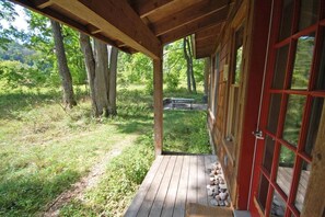 Una cabaña de madera con un porche, una puerta roja y vistas a un bosque.