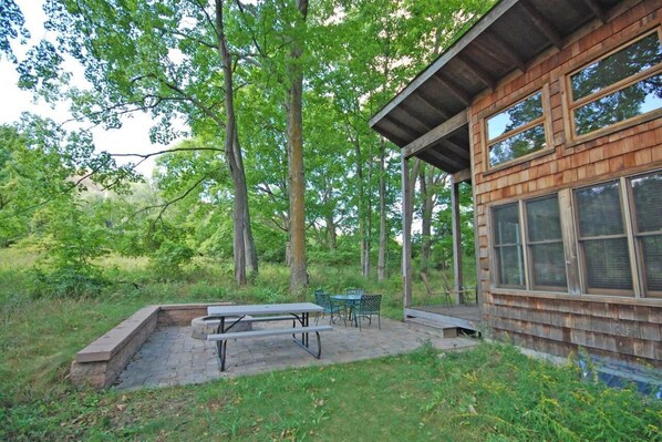 A rustic cabin with a picnic table and chairs in a wooded area.
