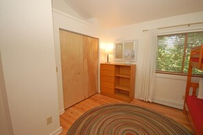 A bedroom with a wooden wardrobe, a bedside table with a lamp, a mirror, a window with curtains, and a bed.