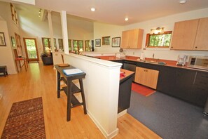 A modern kitchen with wooden cabinets, a central island, and a dining area with a long table and chairs. - Dune Path -  with Waterfront! (Empire)