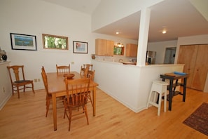 A dining area with a wooden table and chairs, a kitchen with wooden cabinets, and framed pictures on the wall. - Dune Path -  with Waterfront! (Empire)