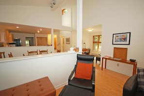 A spacious living area with a large mirror reflecting the kitchen and dining area. There is a black leather chair with an orange cushion, a wooden bench, and a wooden table with a bowl and magazines. - Dune Path - with Waterfront! (Empire)
