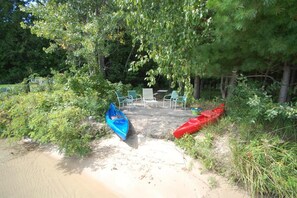 A sandy beach area with a row of green chairs and a table, surrounded by trees.