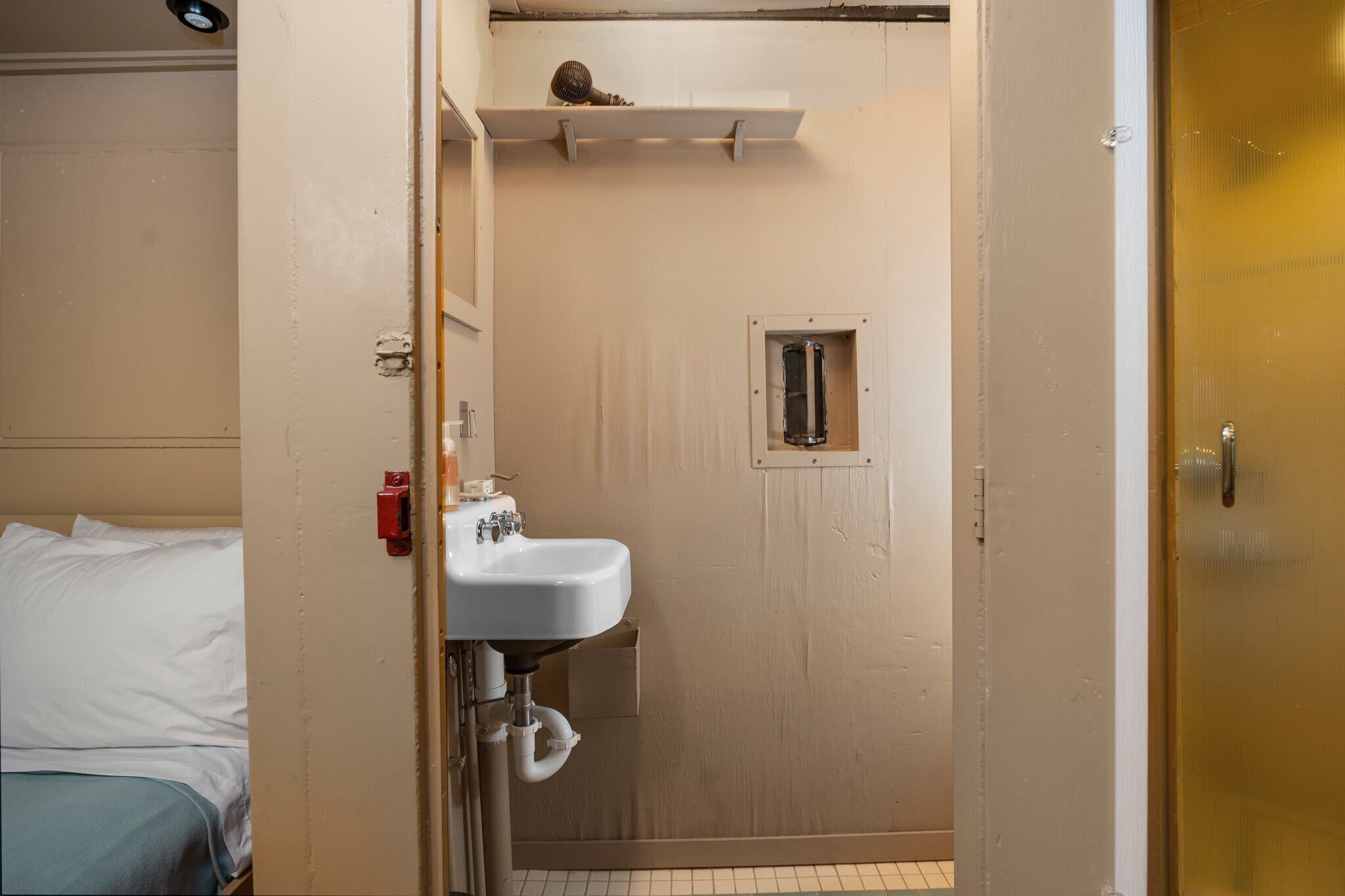 A small, compact bathroom with a white sink, a mirror, and a shower area.