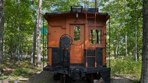 Un vagón de tren antiguo con la inscripción 'DTT 107' y 'BEND', ubicado en un área boscosa.