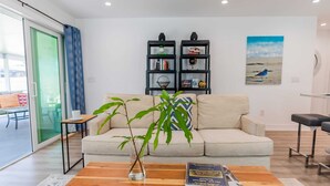 Ein Wohnzimmer mit einer Couch, einem Couchtisch mit einem Buch, einem Bücherregal und einem Gemälde an der Wand.
