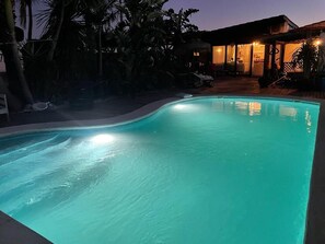 A swimming pool at dusk with a house in the background.