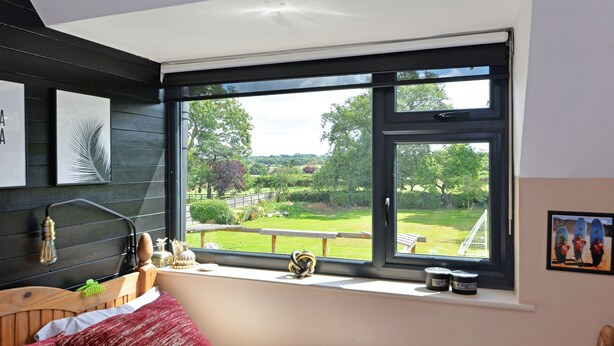 Une chambre avec une grande fenêtre, une tête de lit en bois et une vue sur un jardin.