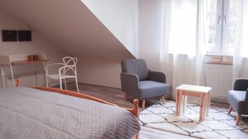 A bedroom with a bed, a desk, two chairs, a small table, and a window with curtains.