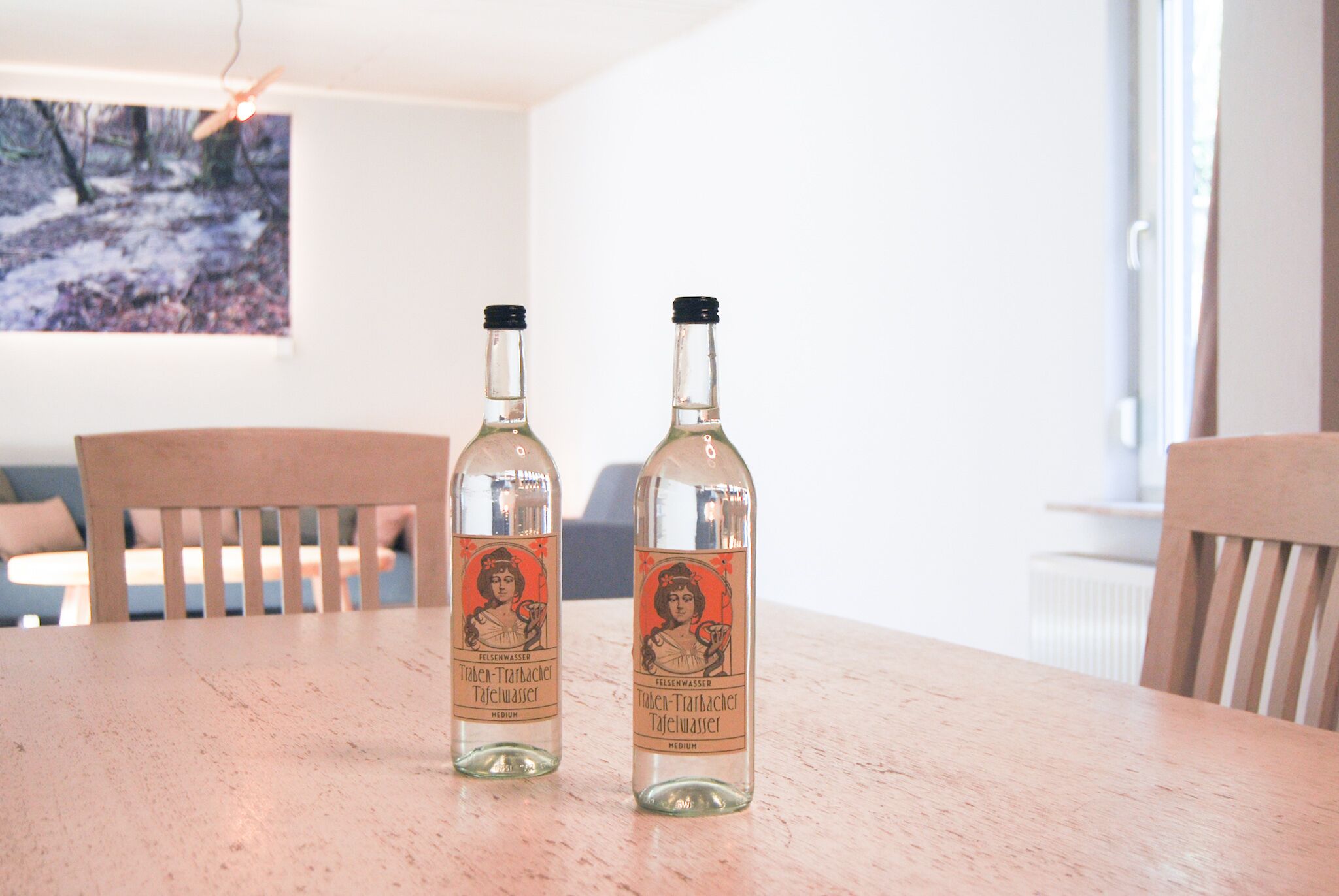 Two bottles of Tafelwasser on a wooden table in a room with a painting on the wall.