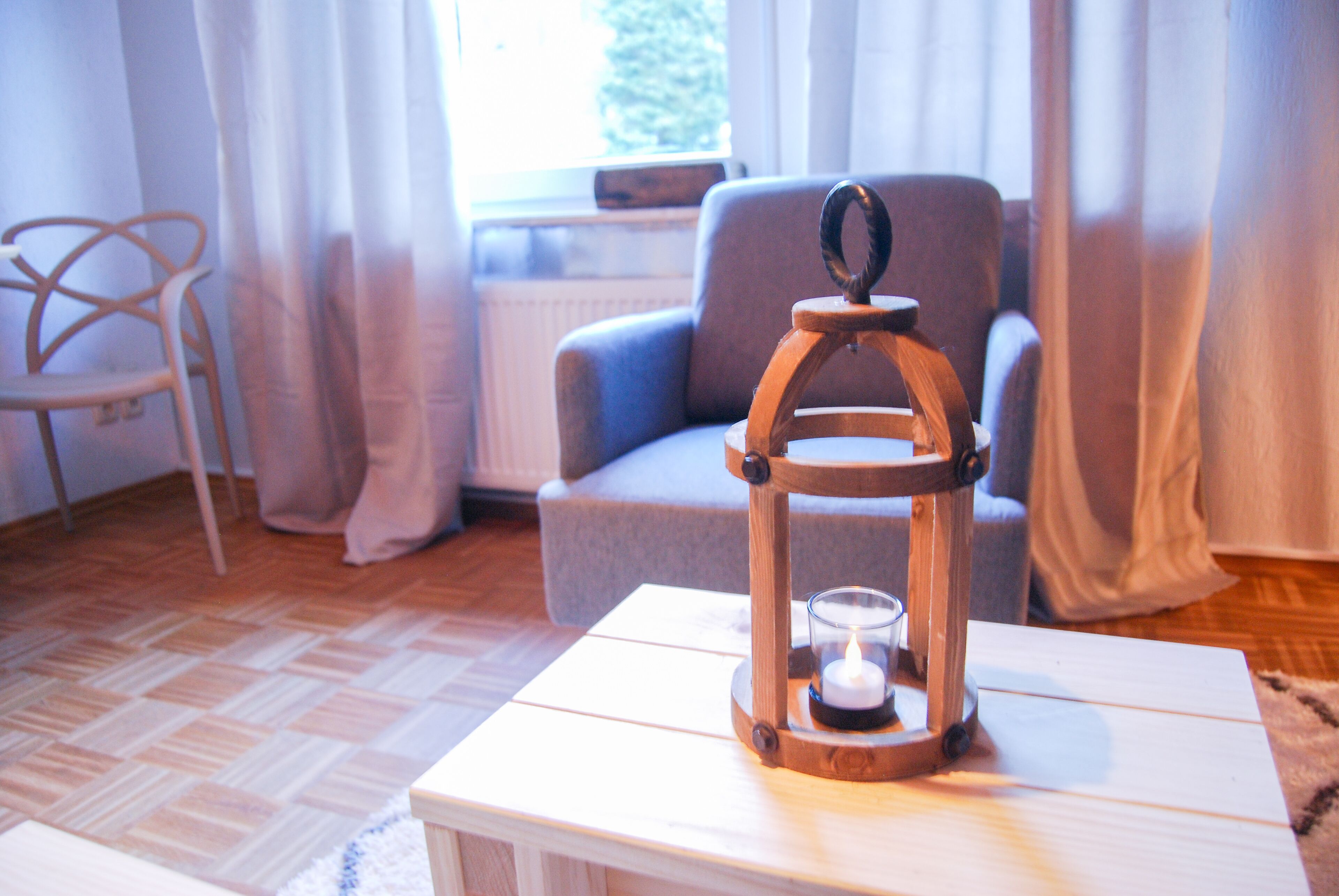 A cozy room with a wooden table, a chair, a lamp, and a window with curtains.
