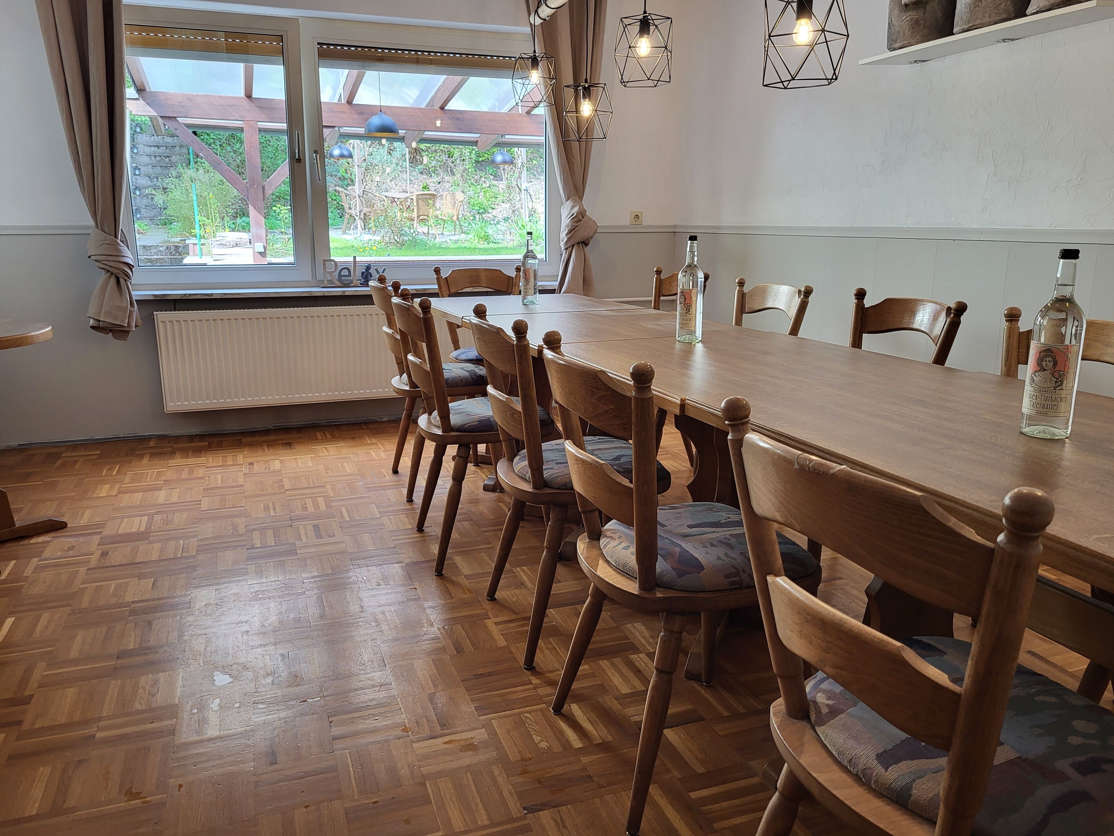 A dining area with a long wooden table, six wooden chairs with cushioned seats, and a window with curtains.