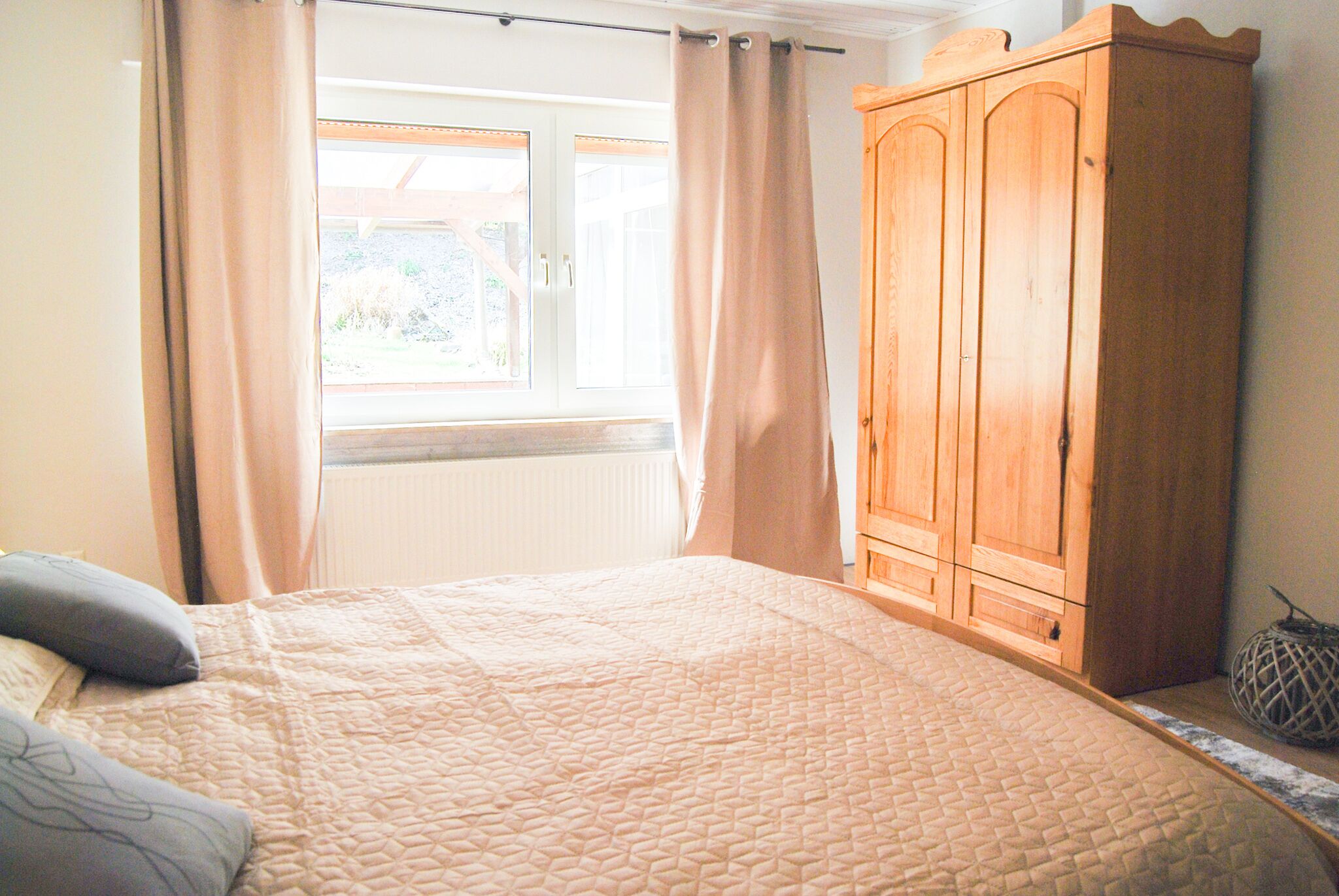 A bedroom with a bed, a wooden wardrobe, and a window with curtains.