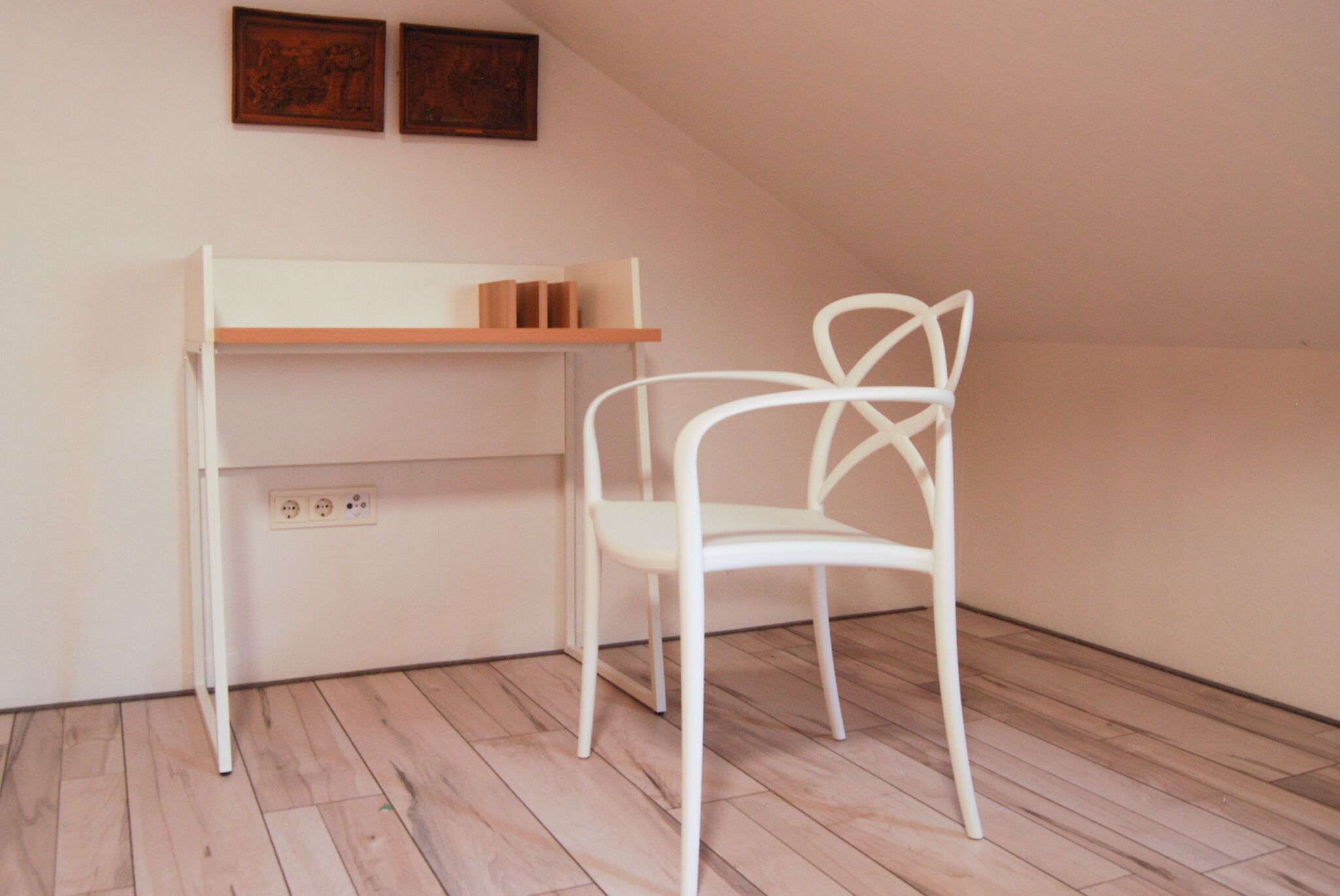 A white desk with a wooden shelf and a white chair in a room with wooden flooring and a sloped ceiling.