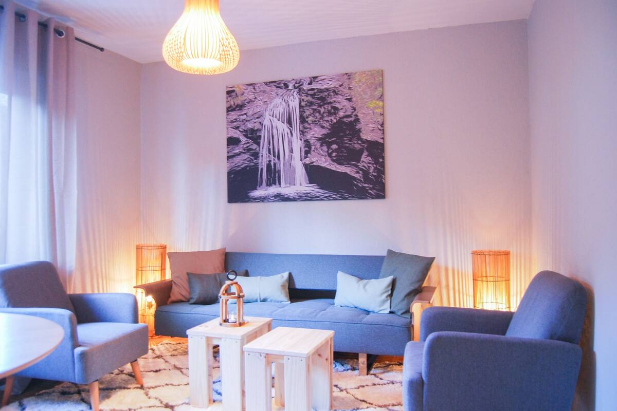 Un salon moderne avec un canapé bleu, deux fauteuils, une table basse et un tableau représentant une cascade accroché au mur.