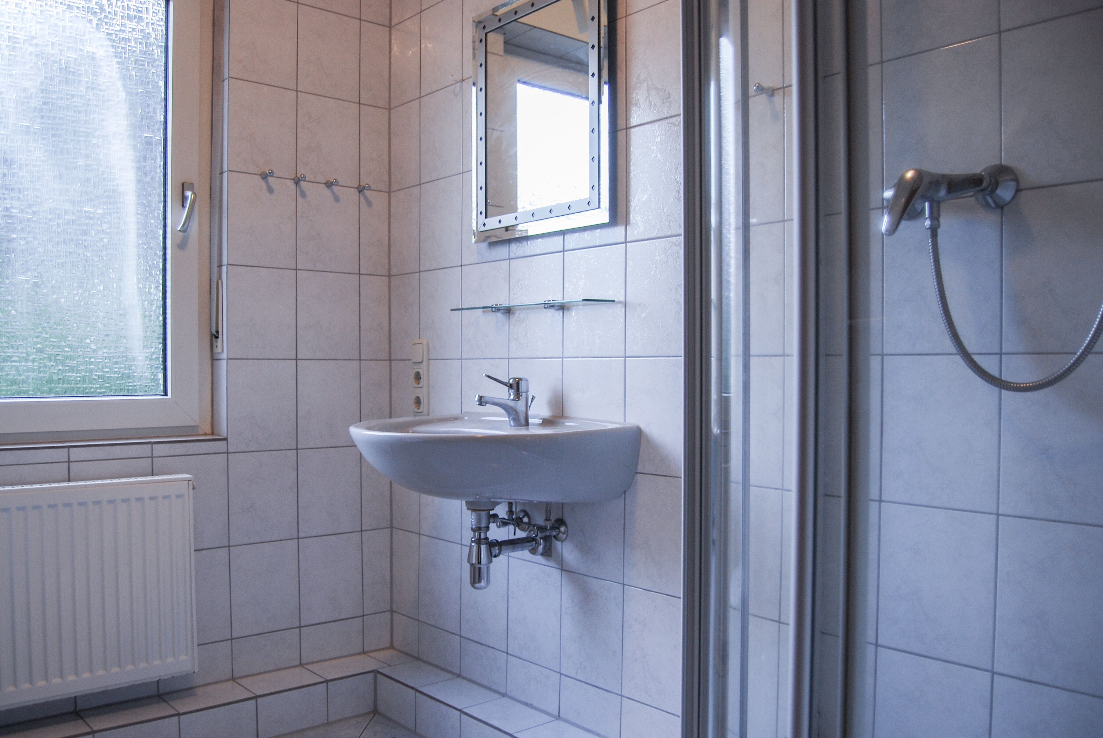 Un baño con lavamanos blanco, espejo y ducha.
