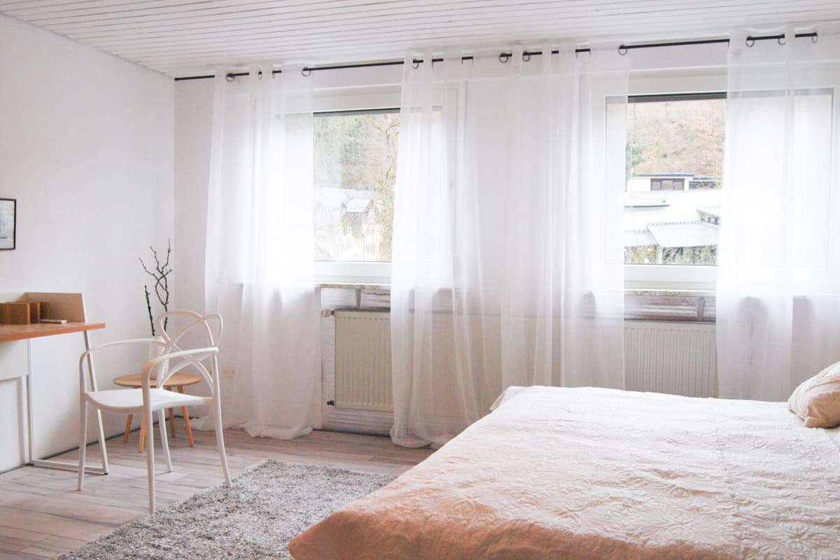 Une chambre à coucher avec un lit, une chaise, un bureau et une fenêtre avec des rideaux.