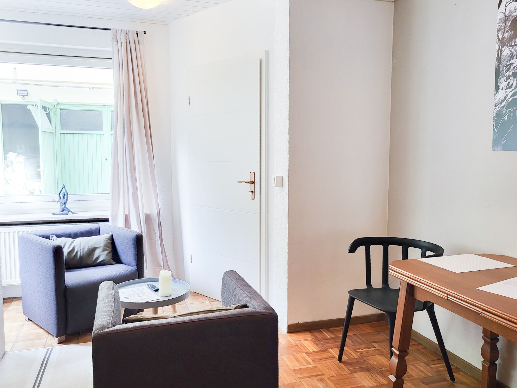 A room with a sofa, a small table with a candle, a wooden chair, and a dining table.