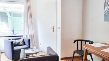 A room with a sofa, a small table with a candle, a wooden chair, and a dining table.