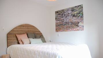 A bedroom with a bed, pillows, a headboard, a wall-mounted painting, and a wooden floor.
