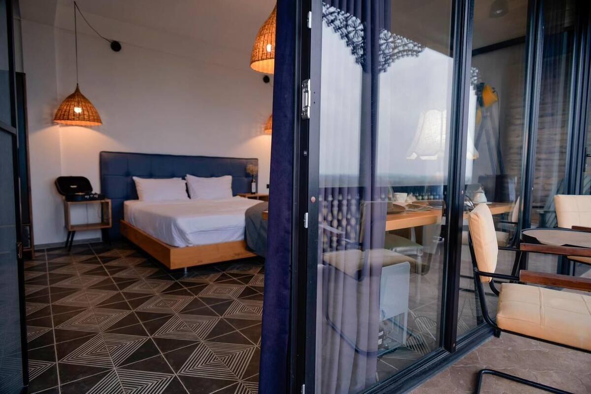 A modern hotel room with a large bed, a desk, and a view through a glass door.