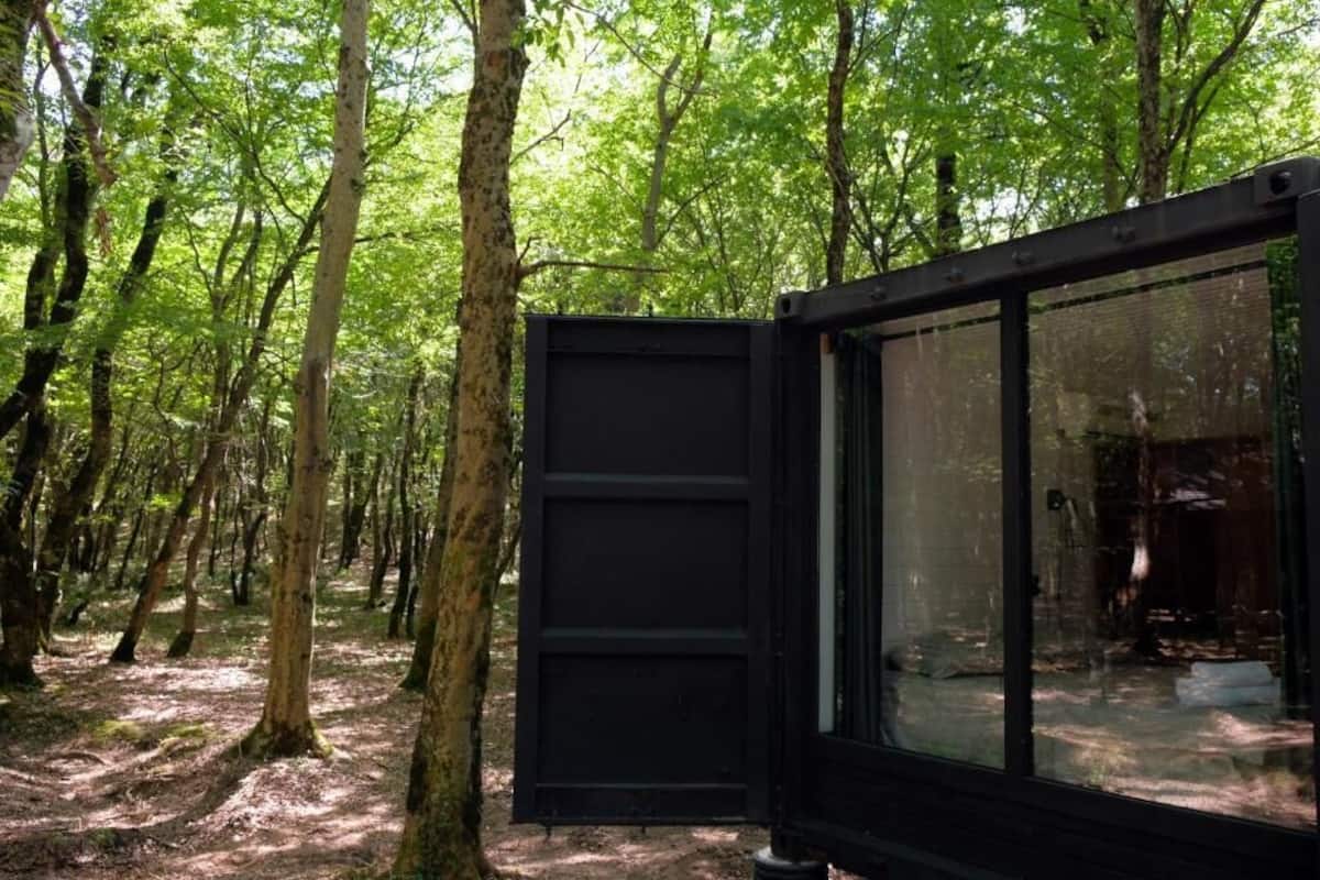 A modern, black-framed glass room with a view of a forested area.