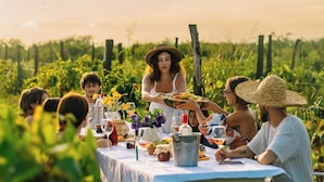 A group of people dining outdoors at a table set with various dishes and drinks, surrounded by greenery. - Chateau Vartsikhe  (Baghdati)