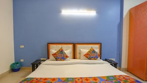 A bedroom with a bed, two pillows, a nightstand, a trash bin, and a wall-mounted light fixture. - Hotel Earthview II  (Noida)
