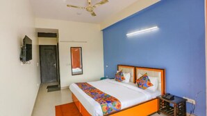 A bedroom with a bed, a ceiling fan, a TV, and a door. - Hotel Earthview II  (Noida)