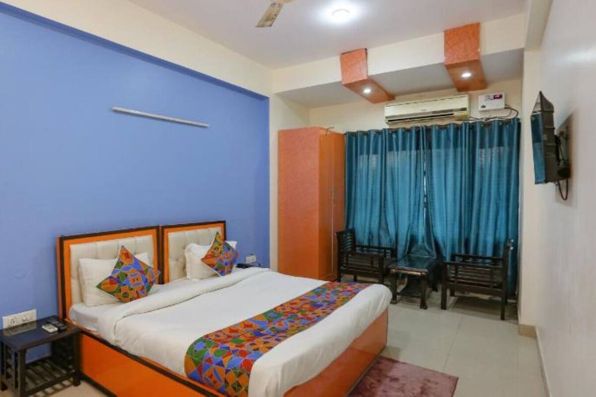 A hotel room with a bed, a desk, a chair, and an air conditioning unit.