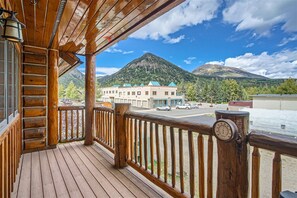 A wooden deck with a view of a mountain and a building with a green roof.