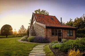 Een huis met een schuin dak, stenen fundering en een stenen pad dat naar de ingang leidt.