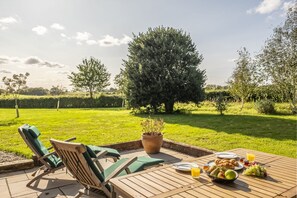 Een terras met een tafel gedekt voor het ontbijt, inclusief borden, fruit en sap.