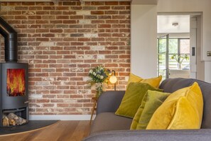 Un salon avec un mur en briques, une cheminée, un canapé avec des coussins jaunes et un vase rempli de fleurs.