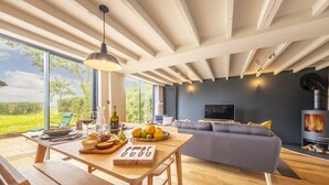 Una sala de estar moderna con un ventanal grande, una mesa de comedor con frutas y queso, un sofá gris y una chimenea.