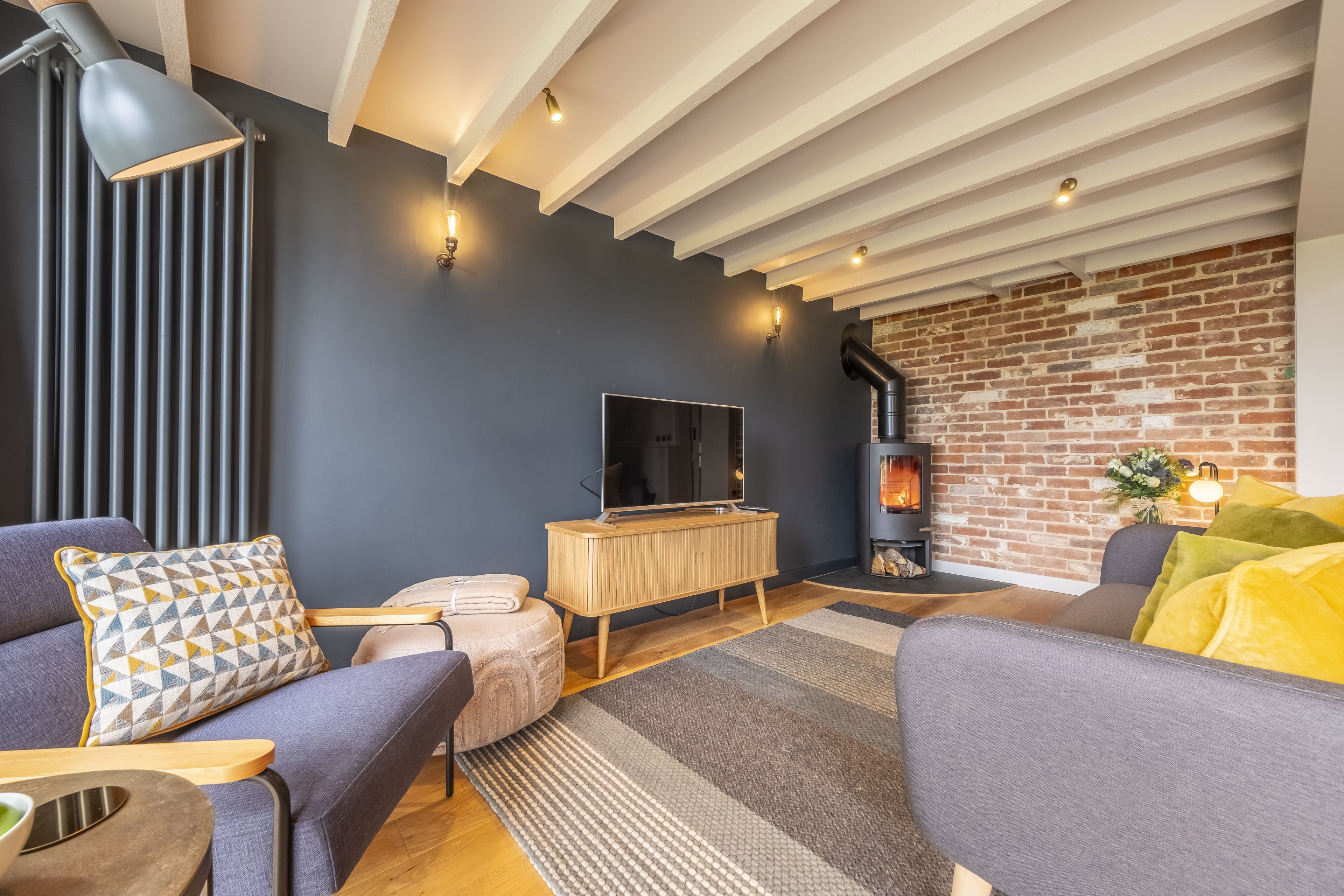 A modern living room with a dark blue wall, a wooden TV stand, a fireplace, and a large window.