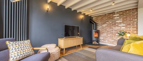 A modern living room with a dark blue wall, a wooden TV stand, a fireplace, and a large window.
