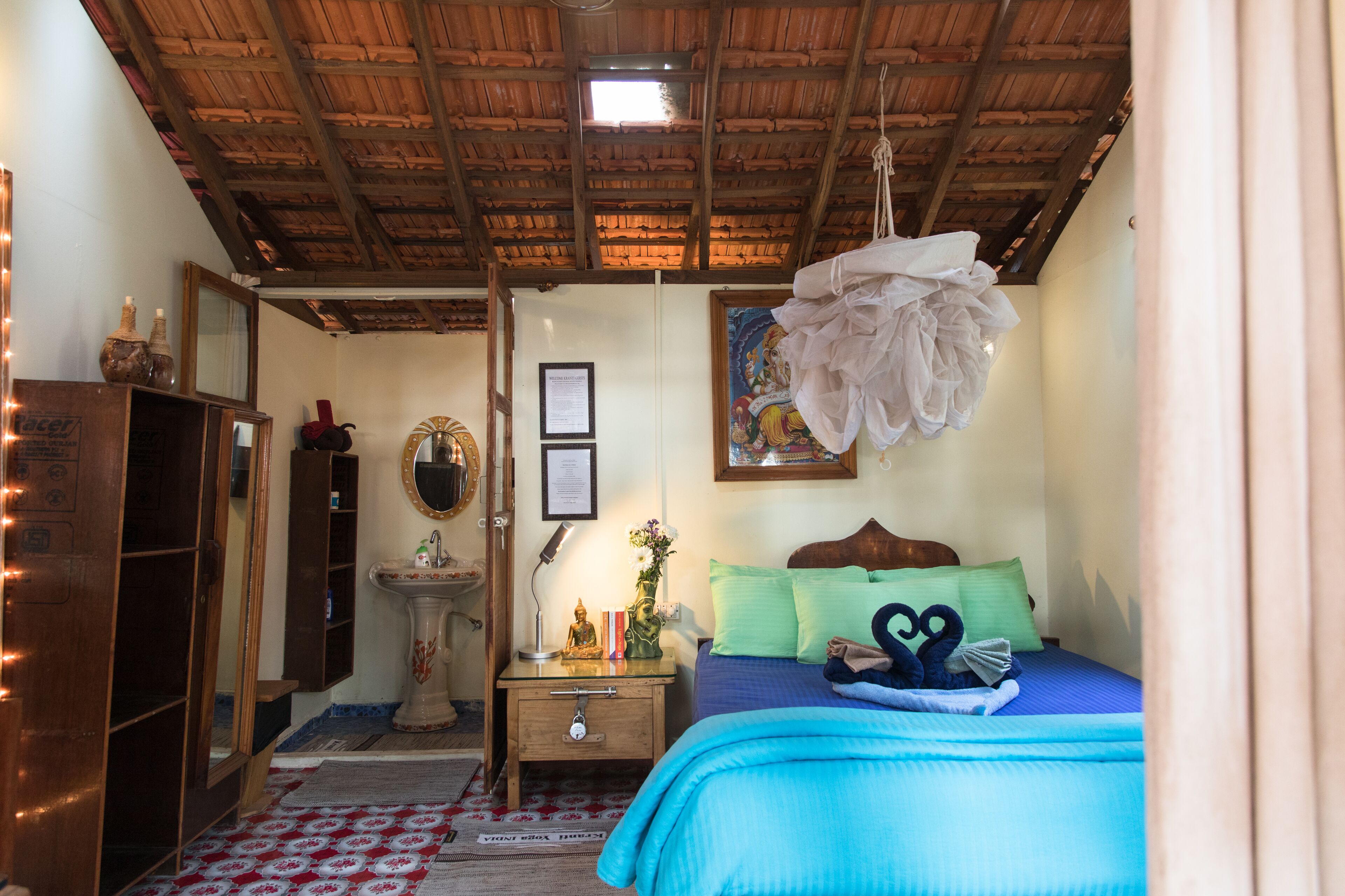 Una habitación con techo de madera, una cama con ropa de cama azul, una mesita de noche con lámpara, un espejo y una pequeña estatua.