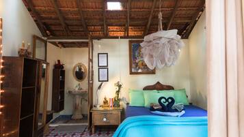 Una habitación con techo de madera, una cama con ropa de cama azul, una mesita de noche con lámpara, un espejo y una pequeña estatua.
