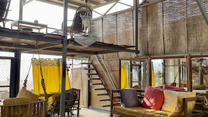 A spacious, open-air lounge with a high ceiling, a hanging chandelier, and a staircase leading to an upper level. - Kranti Yoga Tradition (Canacona)