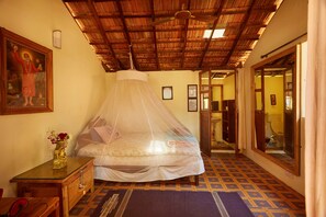 A room with a bed under a mosquito net, a wooden ceiling, a mirror, and a door leading to another room. - Kranti Yoga Tradition (Canacona)