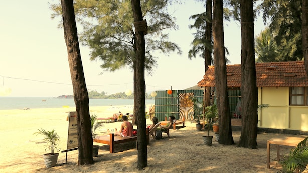 A beachside setting with a wooden bench, potted plants, and a building with a tiled roof. - Kranti Yoga Tradition (Canacona)