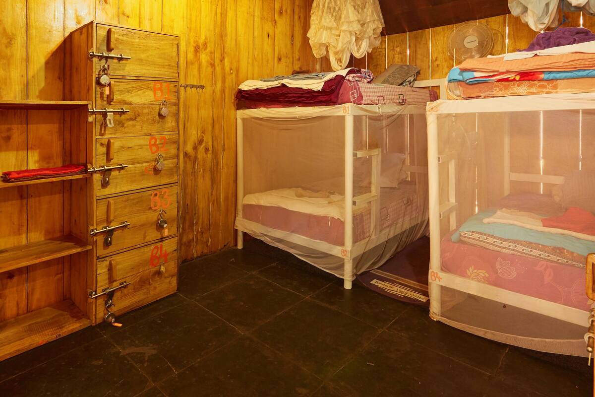 Ein Zimmer mit Holzwänden, einer Kommode, zwei Stockbetten mit Moskitonetz und einem Ventilator rechts.