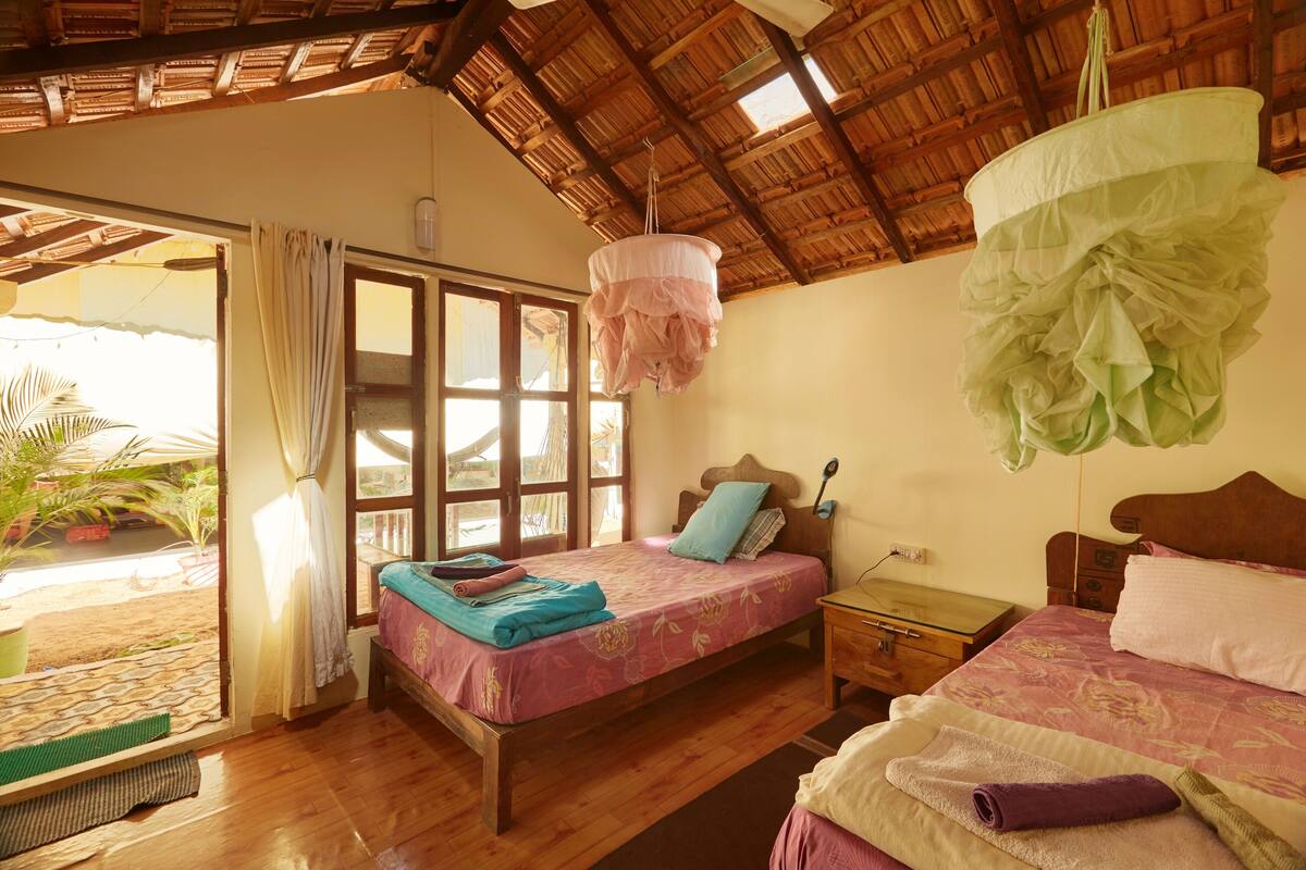 Ein Schlafzimmer mit einem hölzernen Bett, einem Nachttisch, einer Pendelleuchte und Blick ins Freie.